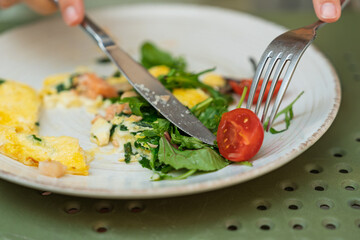 A person's hands cutting a fresh tomato while eating a delicious omelette for breakfast