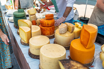Large delicious wheels of yellow, orange, and green craft cheese for sale at an authentic street market