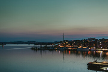 Naklejka premium Oslo harbour at dusk transforms into a mesmerising scene, with long-exposure capturing the vibrant night lights reflecting on the calm water
