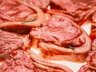 Premium quality marinated lamb loin chops and rosemary herb on white background. Uncooked raw meat on the bone in red color water based marinade to enhance dish taste.