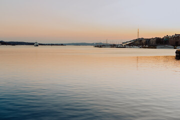Fototapeta premium Bathed in the warm glow of sunset, Oslo harbour showcases traditional colourful wooden houses along the waterfront, with boats gently berthed in the distance.