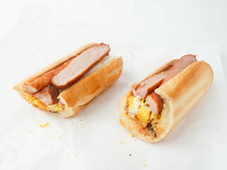 Traditional tasty Irish breakfast roll with white bread, sausage, bacon or rasher, fried egg and black pudding on greasy wrapping paper. Popular high calorie meal in Ireland. Classic dish