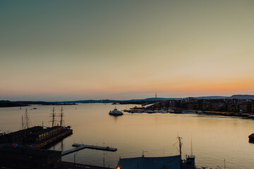 A vibrant sunset bathes the Astrup Fearnley Museum of Modern Art in Oslo, with a ferry gracefully sailing by, creating a harmonious blend of art, architecture, and the beauty of the Oslofjord