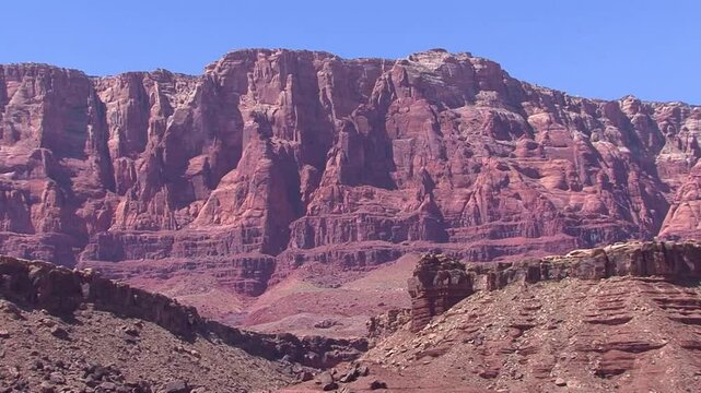 LTR pan of massive red sandstone cliffs under a blue sky in the Mogollon Rim region between the Grand Canyon and Page, Arizona.