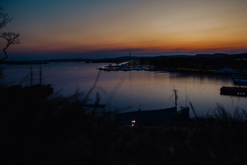 A vibrant sunset bathes the Astrup Fearnley Museum of Modern Art in Oslo, with a ferry gracefully sailing by, creating a harmonious blend of art, architecture, and the beauty of the Oslofjord