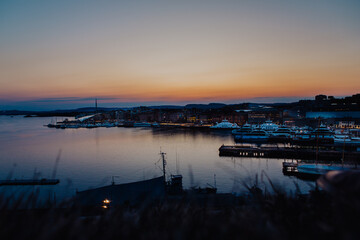 A vibrant sunset bathes the Astrup Fearnley Museum of Modern Art in Oslo, with a ferry gracefully sailing by, creating a harmonious blend of art, architecture, and the beauty of the Oslofjord