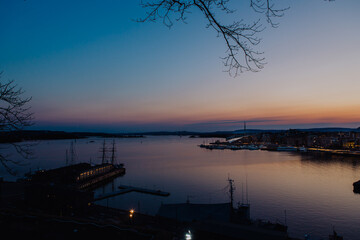 A vibrant sunset bathes the Astrup Fearnley Museum of Modern Art in Oslo, with a ferry gracefully sailing by, creating a harmonious blend of art, architecture, and the beauty of the Oslofjord