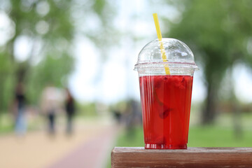 Lemonade in a disposable plastic cup, takeaway drink. Refreshing drink against the background of a park in summer. Pink lemonade with raspberries and lime. Close-up of a drink in a disposable cup