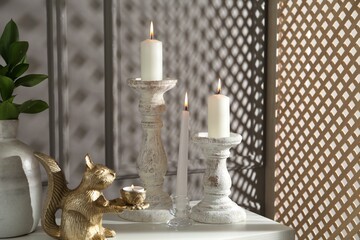 Elegant candlesticks with burning candles, branches in vase and other decor on dresser near grey...