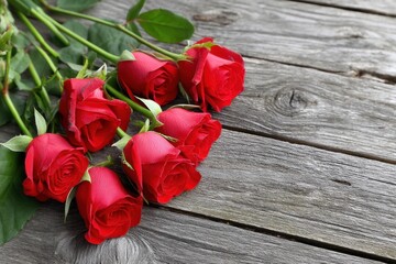 A cluster of fresh red roses lies beautifully on a weathered wooden tabletop. Their rich color and delicate petals evoke feelings of romance, making them ideal for gifting on significant occasions.
