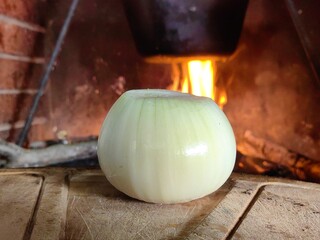 Peeled onion on wooden kitchen board with fire, flame in background