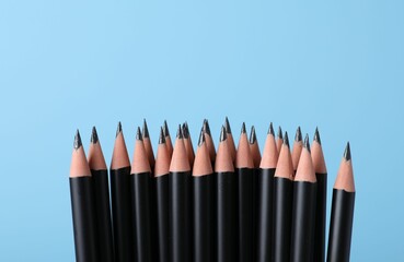 Many sharp graphite pencils on light blue background, closeup. Space for text