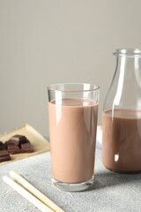 Tasty chocolate milk in glass, bottle and pieces on grey table