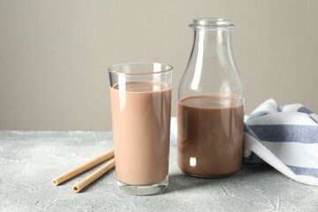 Tasty chocolate milk in glass, bottle and straws on grey table
