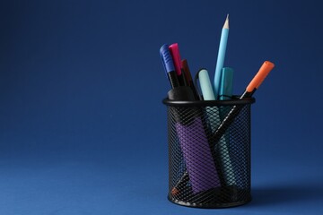 Different stationery in pen holder on dark blue background. Space for text