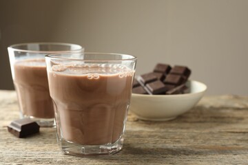 Tasty chocolate milk in glasses and pieces on wooden table, closeup. Space for text