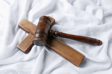 Judge's gavel and wooden cross on white fabric, above view