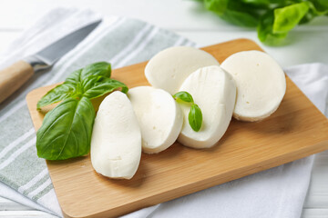 Pieces of delicious mozzarella cheese and basil leaves on white wooden table, closeup