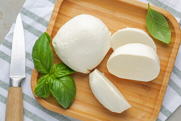Pieces of delicious mozzarella cheese, basil leaves and knife on grey table, top view