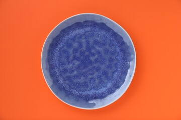 Empty plate on orange background, top view