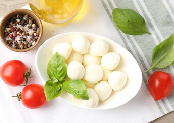 Tasty mozzarella cheese balls, tomatoes, basil, oil and peppercorns on table, flat lay