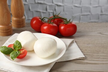 Tasty mozzarella cheese balls, tomatoes and basil on wooden table, closeup. Space for text
