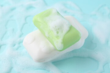 Soap bars with foam on light blue background, closeup