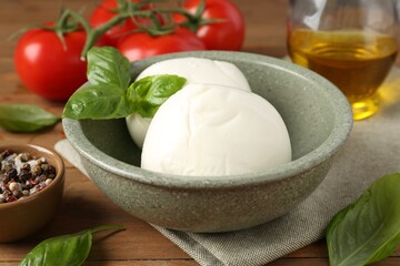 Tasty mozzarella balls, tomatoes, oil and basil on wooden table, closeup