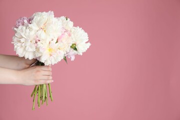 Woman with bouquet of beautiful peonies on pink background, closeup. Space for text