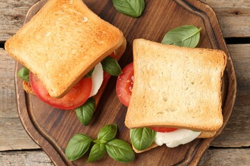Tasty sandwiches with mozzarella cheese, tomatoes and basil on wooden table, top view