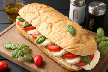 Tasty sandwich with mozzarella cheese, tomatoes and basil on black wooden table, closeup
