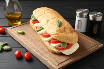 Tasty sandwich with mozzarella cheese, tomatoes and basil on black wooden table, closeup