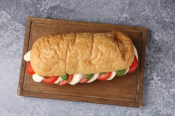 Tasty sandwich with mozzarella cheese, tomatoes and basil on grey textured table, top view