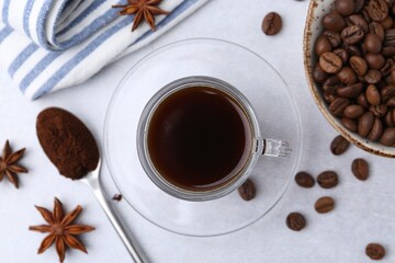 Cup of aromatic coffee, beans and star anise on white table, flat lay