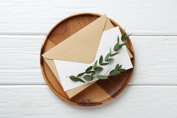 Blank invitation card, envelope, tray and branches on white wooden table, top view