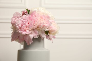 Beautiful peonies in vase near white wall, closeup. Space for text