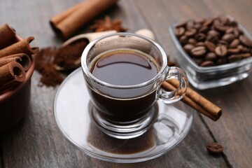 Refreshing coffee in cup and cinnamon stick on wooden table, closeup