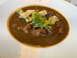 Hearty beef stew with herb garnish and dumplings on a ceramic plate