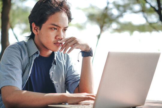 Serious Asian Young businessman work at outdoor with laptop. Concept of remote and freelance work. Young successful man wearing casual blue cloth.