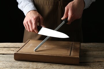 Man sharpening knife with sharpener on wooden table, closeup