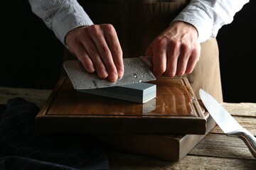 Man sharpening knife with sharpener on wooden table, closeup