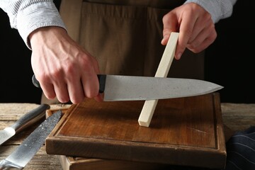 Man sharpening knife with sharpener on wooden table, closeup