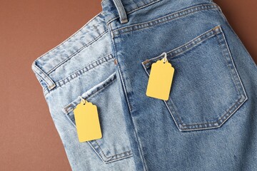 Jeans with tags on brown background, top view
