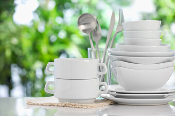 Different clean dishes on white table against blurred green background