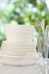 Different clean dishes on white table against blurred green background, closeup