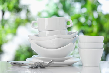 Different clean dishes on white table against blurred green background