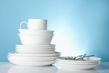 Different clean dishes on white table against light blue background