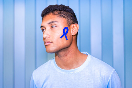Latino man with cancer awareness ribbon on his face, looking thoughtful - Powered by Adobe