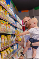 Father together with little son buying children food at supermarket. Little kid reaches to the baby...