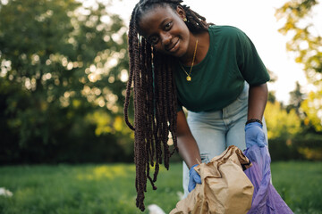 Young woman wearing gloves picking up trash in park